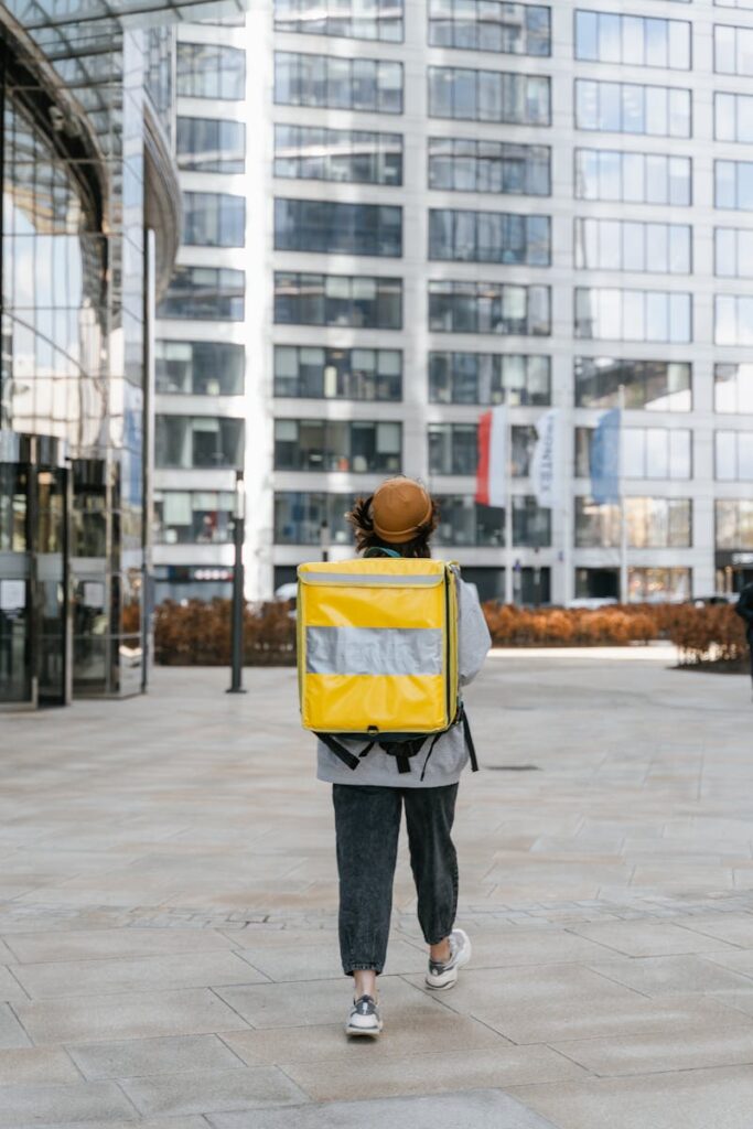 pexels-photo-7706415-7706415 A food delivery person walking downtown with a yellow thermal bag, showcasing urban courier service.